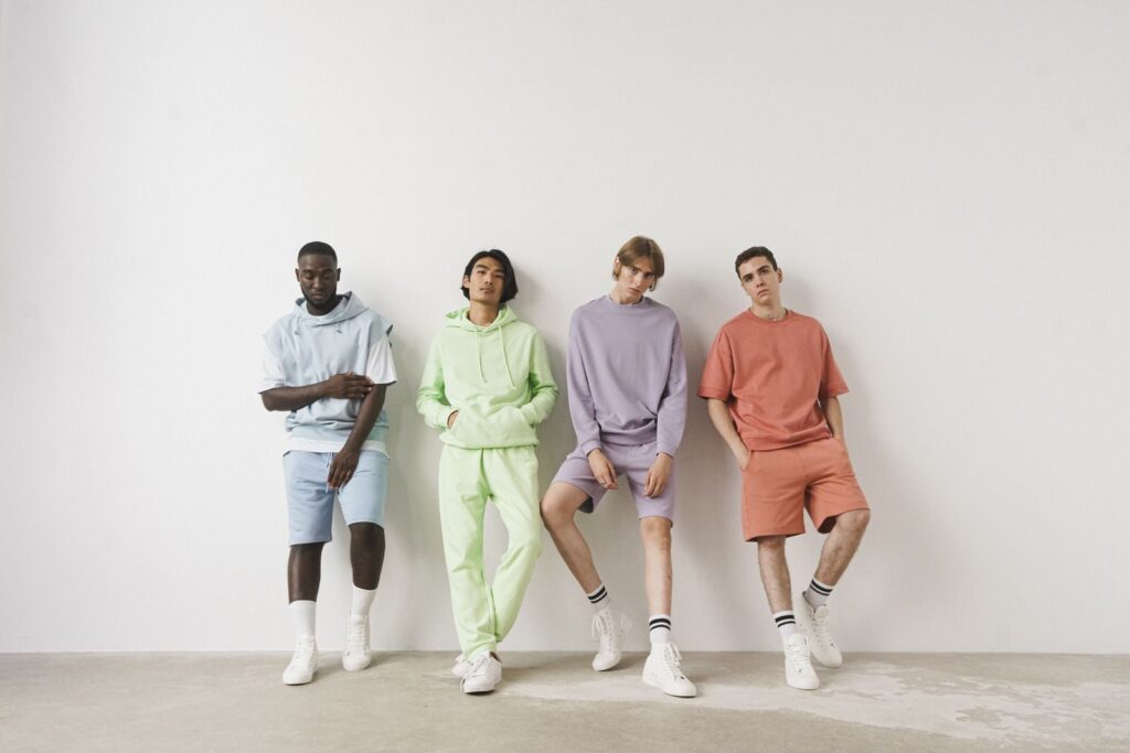 Group of stylish men in colorful pastel outfits posing against a white wall.